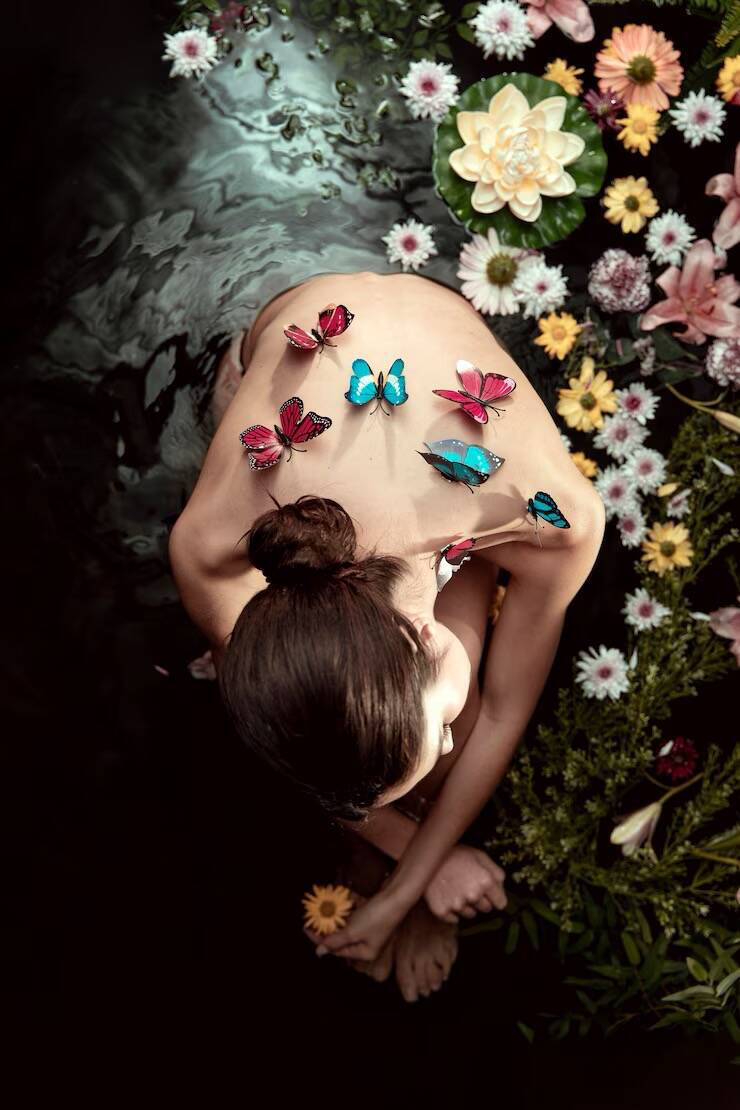 Woman with butterflies on her back surrounded by grass and flowers